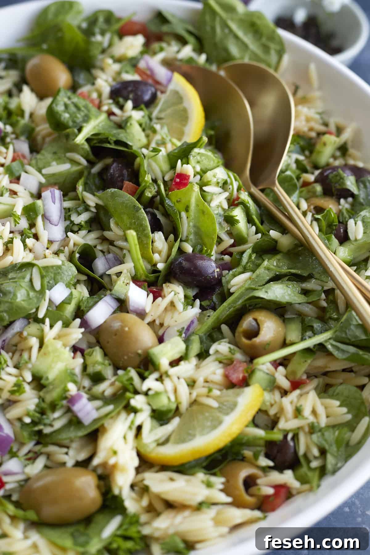 close up image of a bowl of Greek orzo pasta salad with serving spoons