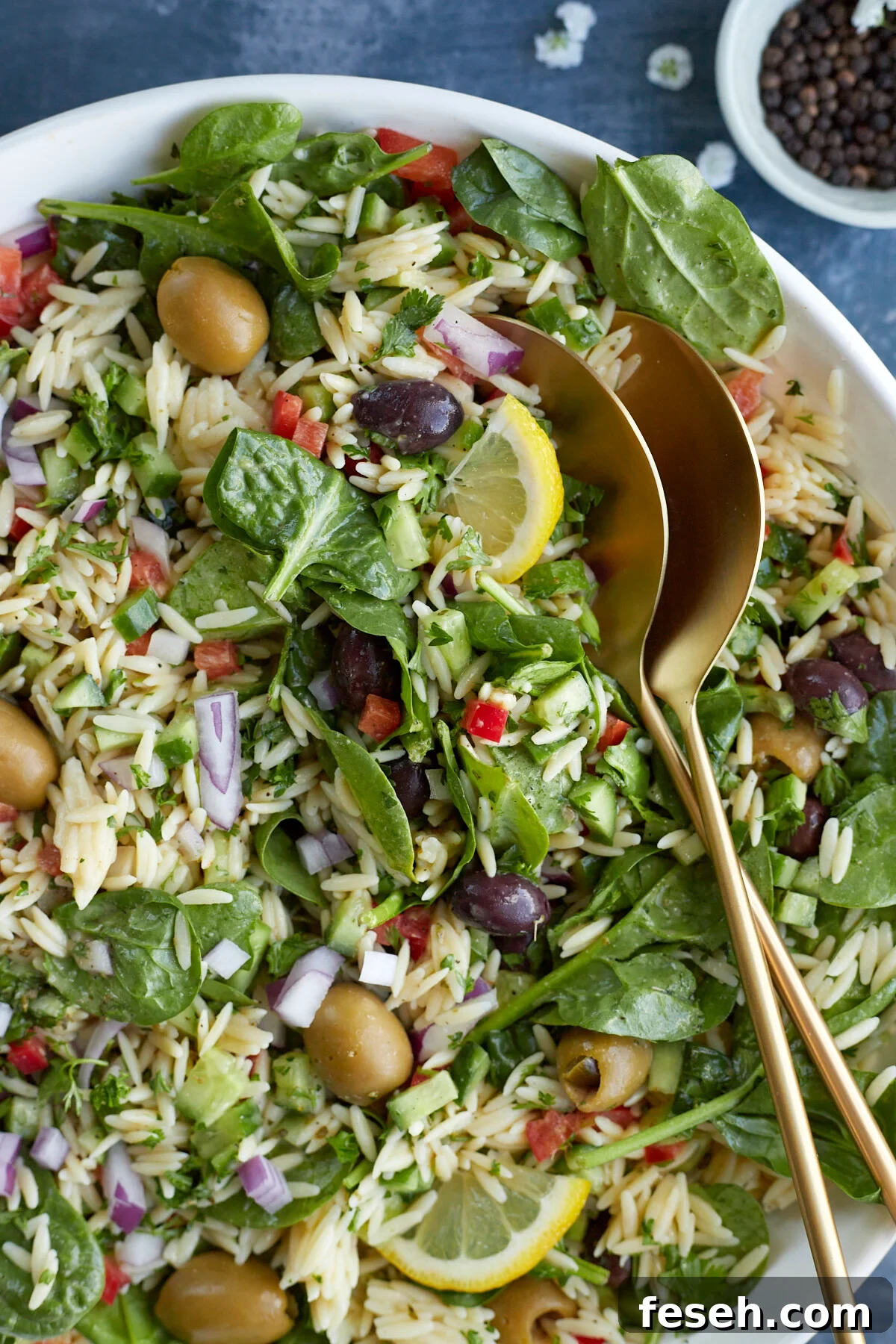 a bowl of Greek orzo pasta salad with two serving spoons on top