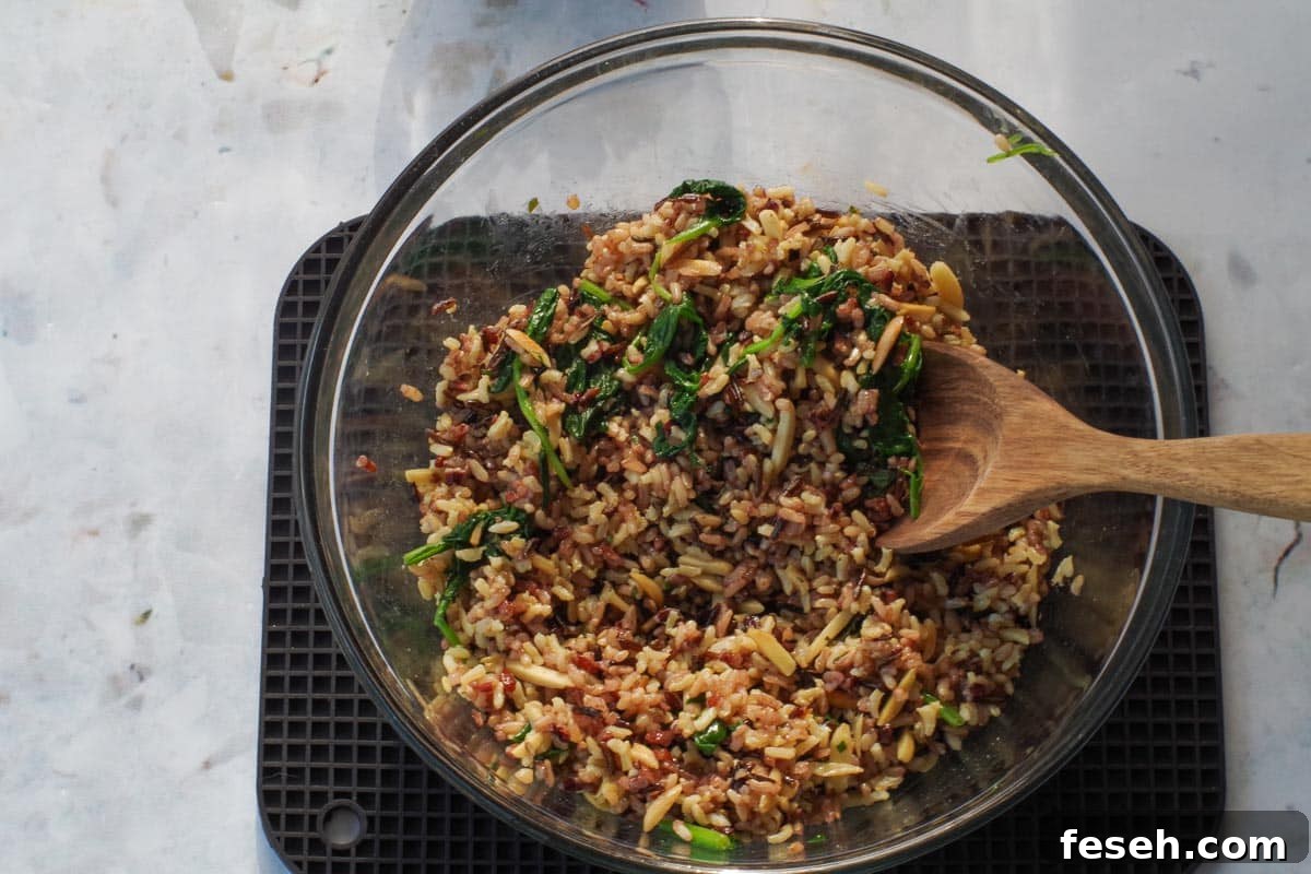 spinach and almonds stirred into rice mixture in glass bowl with wooden spoon