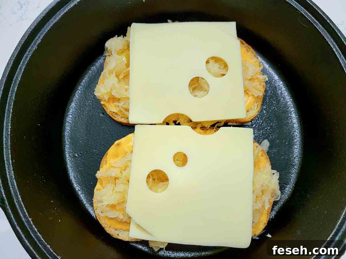 swiss cheese and sauerkraut added to two slices of rye bread in a cast iron skillet.