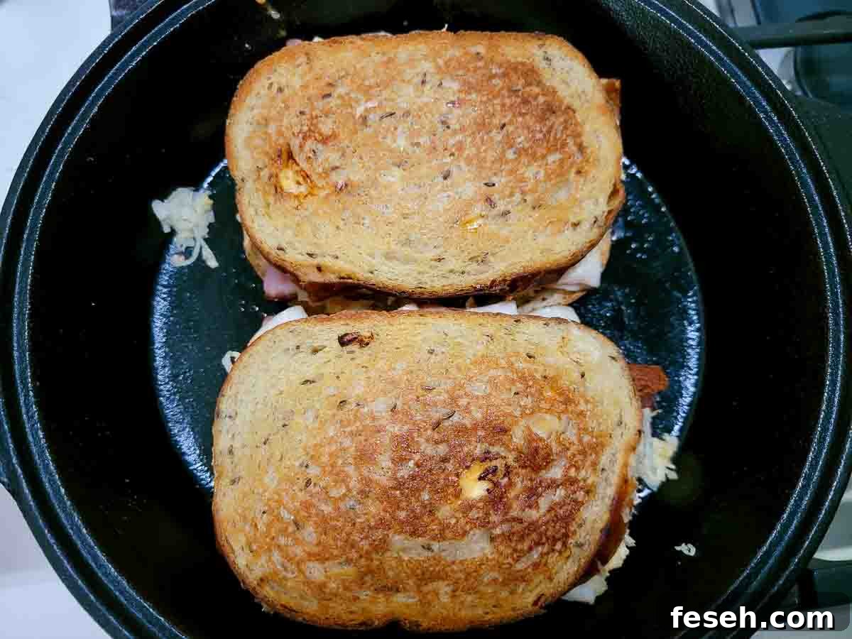Reuben sandwich with ham cooking in a cast iron skillet.