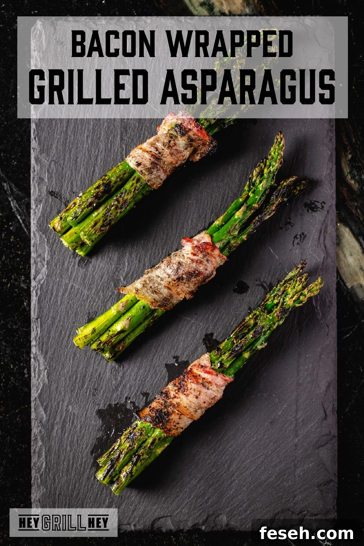 Three bacon-wrapped bundles of asparagus resting on a black plate. The text overlay reads "Bacon Wrapped Grilled Asparagus" at the top, and "Hey Grill Hey" at the bottom.