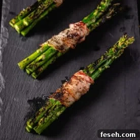 Three bacon-wrapped bundles of asparagus resting on a black plate.