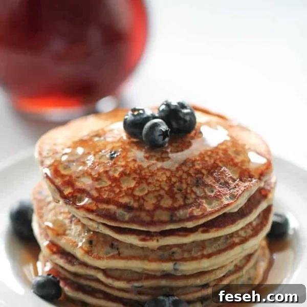 A stack of Blueberry Protein Pancakes on a plate topped with butter and fresh blueberries.