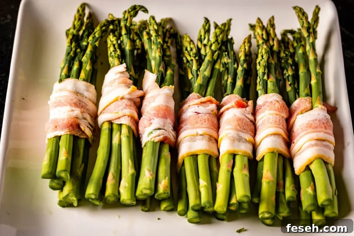 Uncooked bacon around bundles of asparagus on a white platter.