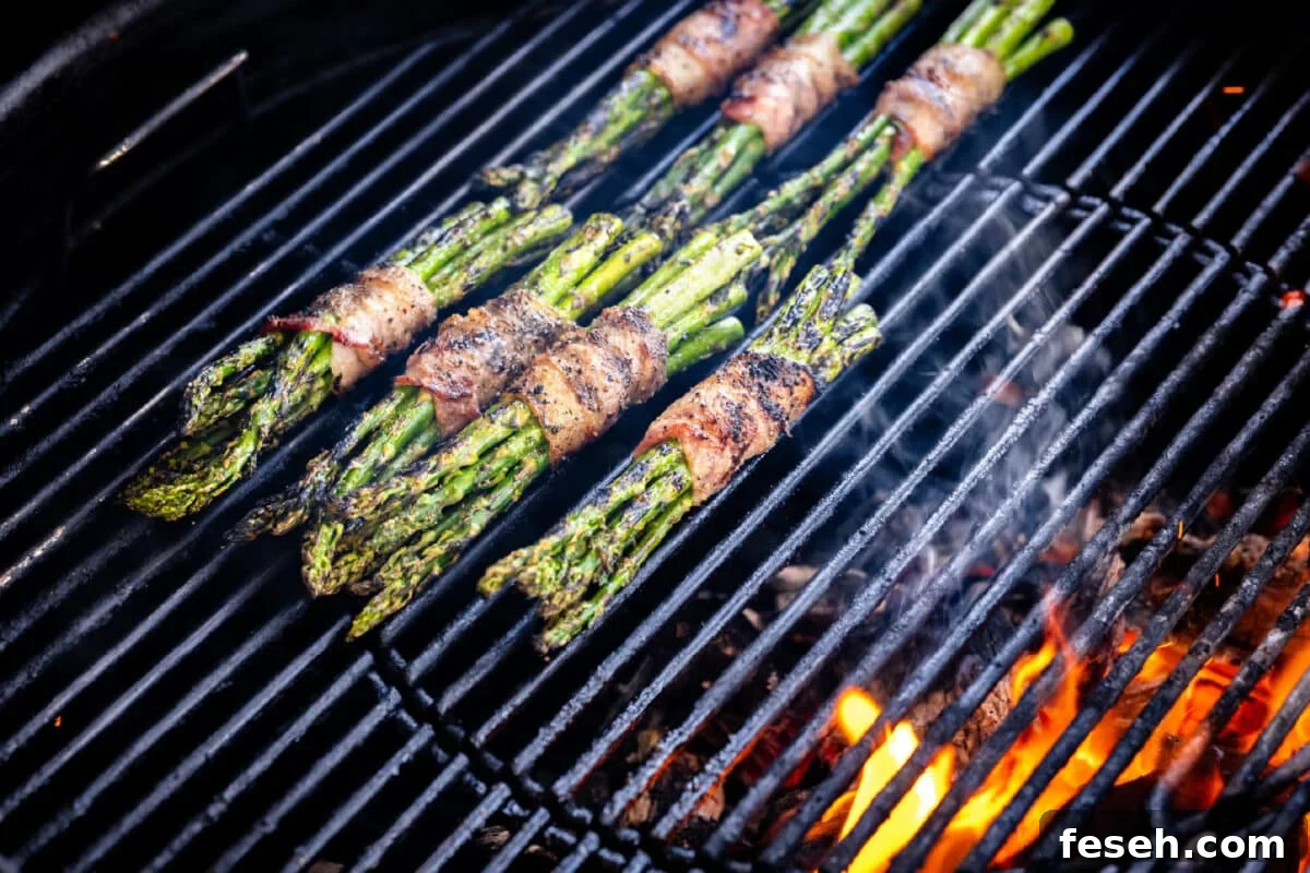Bacon wrapped veggies sitting on the grates of a charcoal grill over a flame.