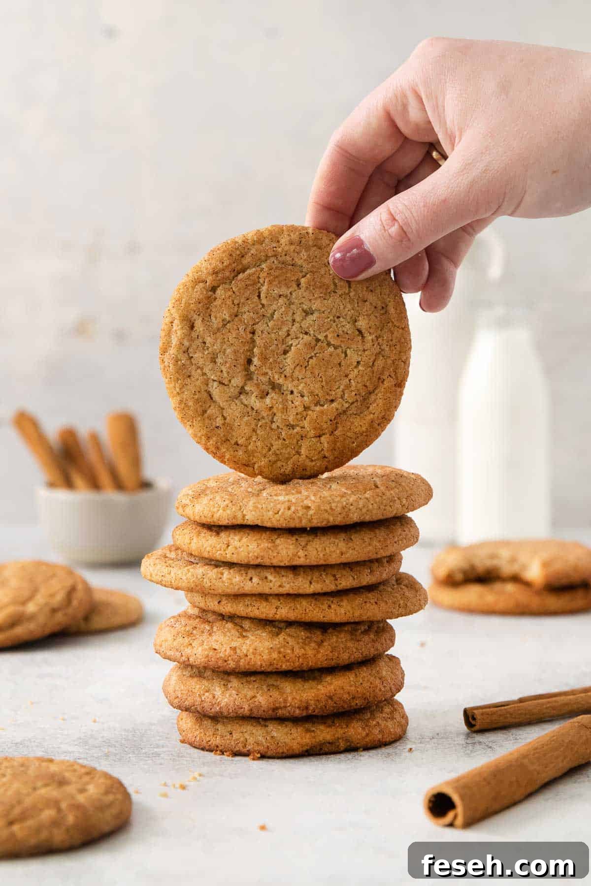 almond flour snickerdoodles stacked on top of each other, and a hand reaching for the top cookie