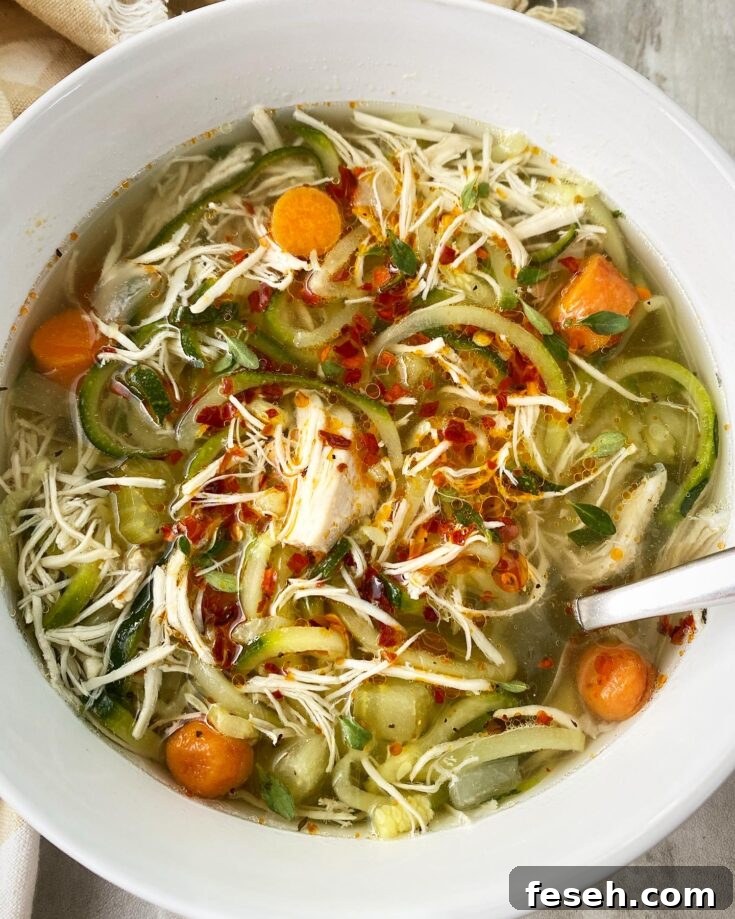 overhead shot of slow cooker chicken zoodle soup in a white bowl garnished with chili oil