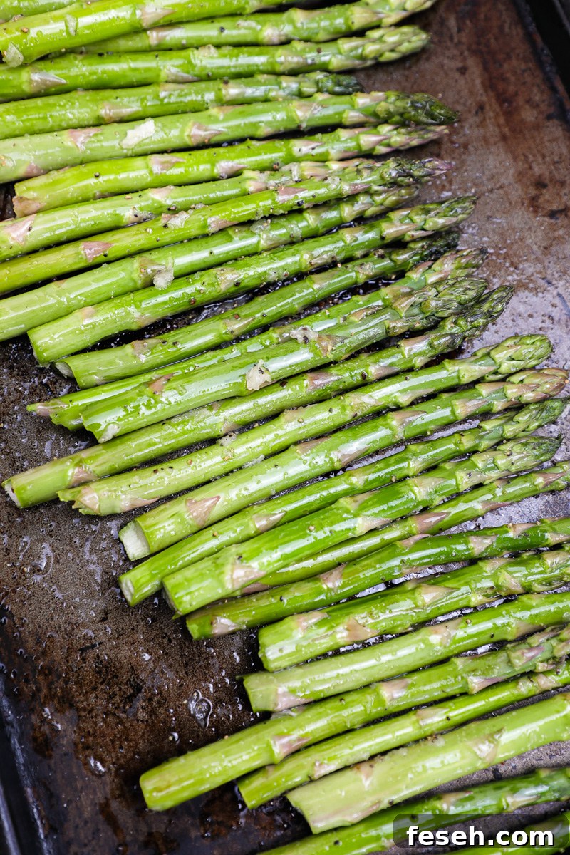 Fresh asparagus is tossed with olive oil, garlic, salt and papper and spread out on a dark baking pan