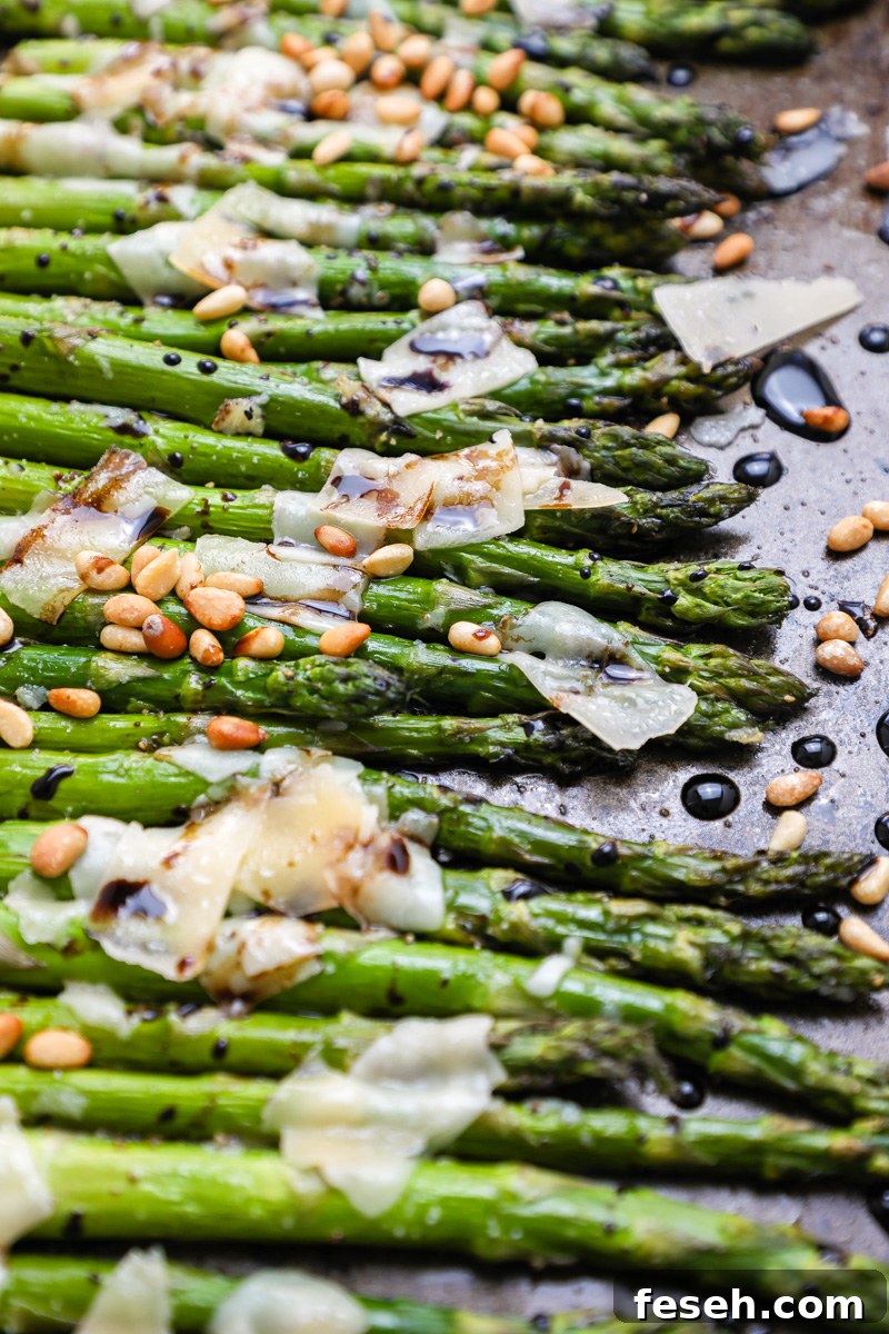 A close up photo of roasted asparagus topped with shaved parmesan and toasted pine nuts