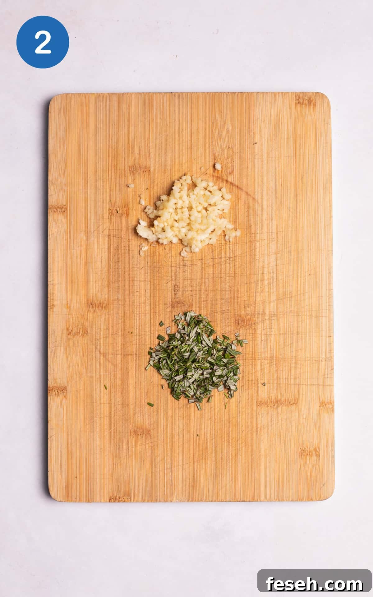 crushed garlic cloves and diced fresh rosemary on a cutting board.