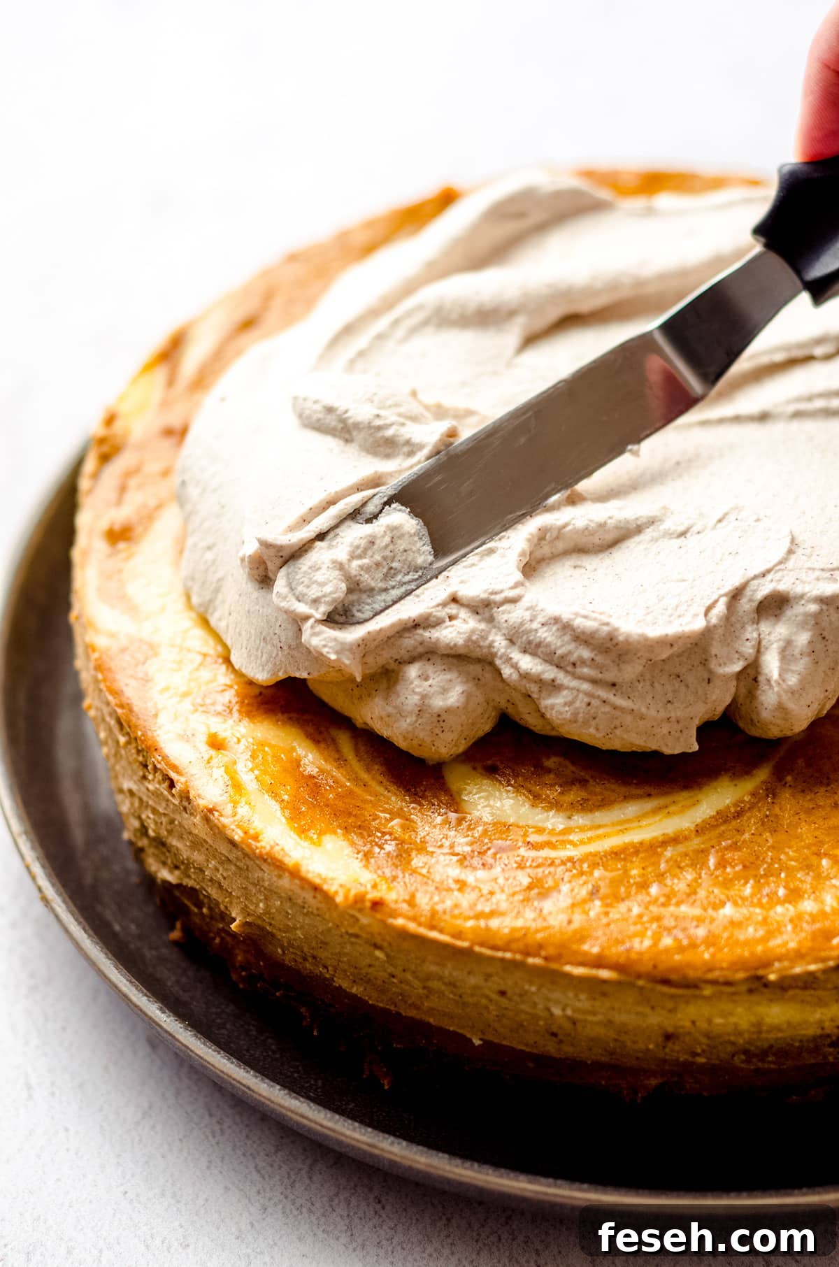 an offset spatula spreading pumpkin spiced whipped cream onto a pumpkin cheesecake