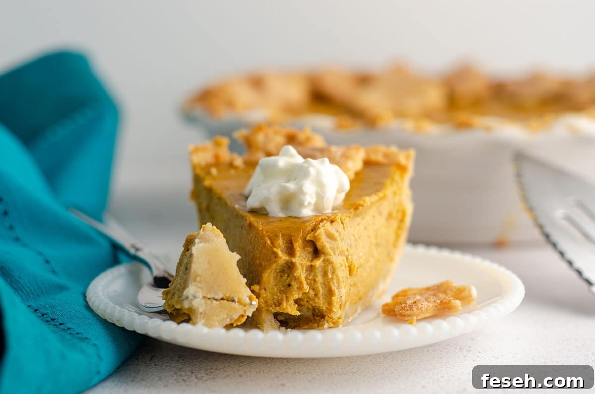 bite taken out of a slice of pumpkin pie with a dollop of whipped cream on a plate with a fork