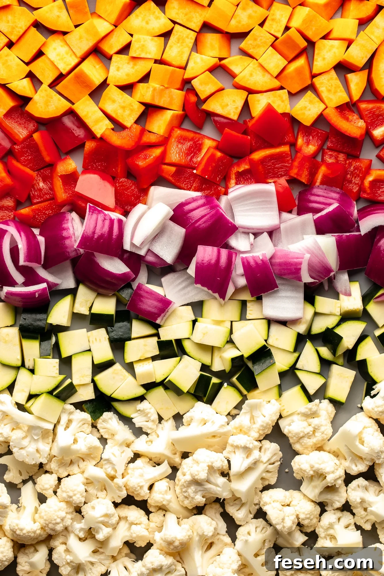 overhead view of a medley of raw chopped vegetables on a sheet pan.