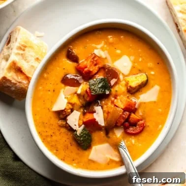 overhead view of a bowl of roasted vegetable soup topped with roasted vegetables with a piece of bread on the side.