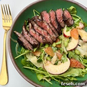 A green bowl filled with a fresh salad topped with slices of medium-rare steak