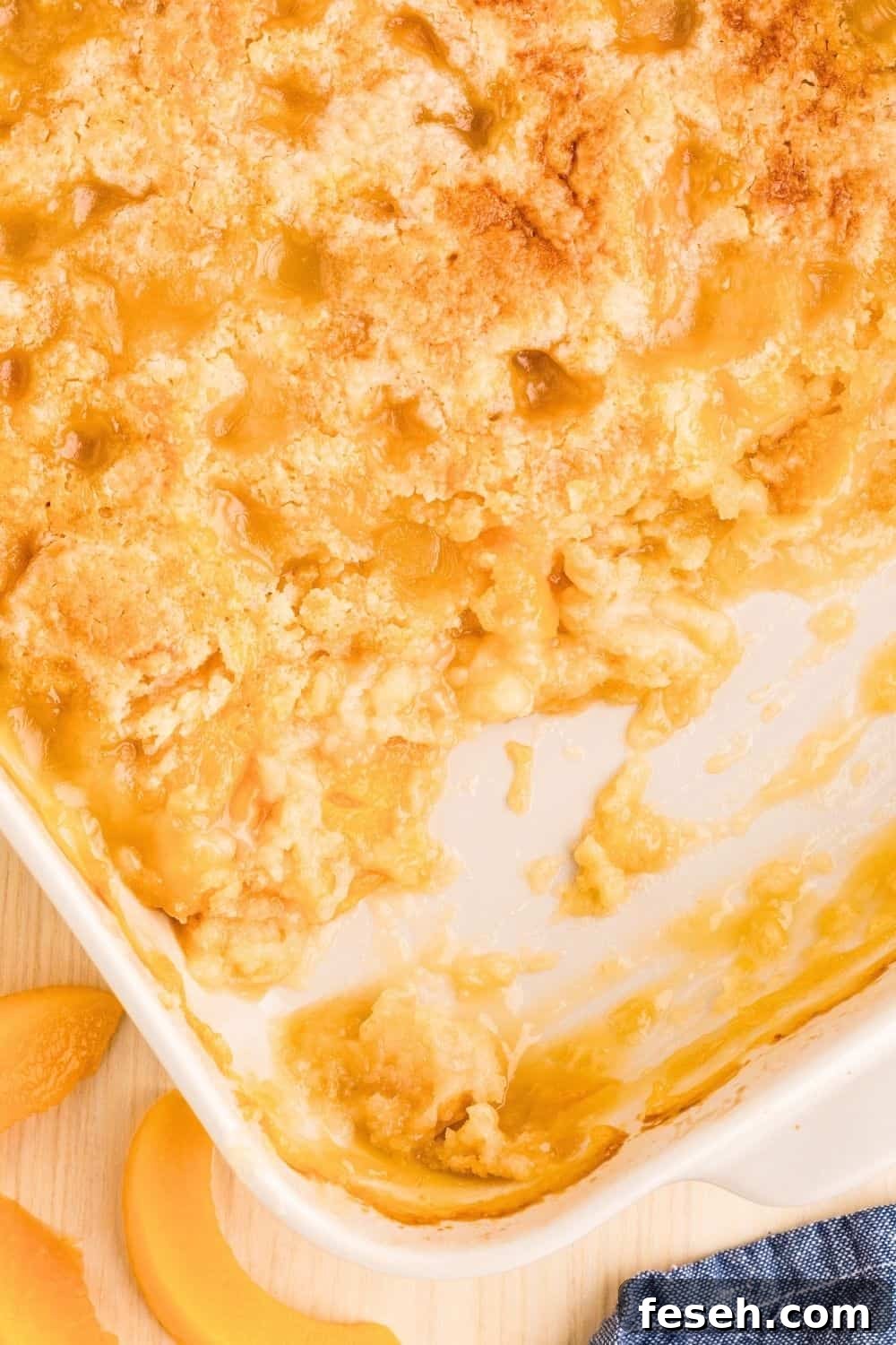 overhead view of a white baking dish of peach dump cake, with some of the dump cake scooped out of the dish.