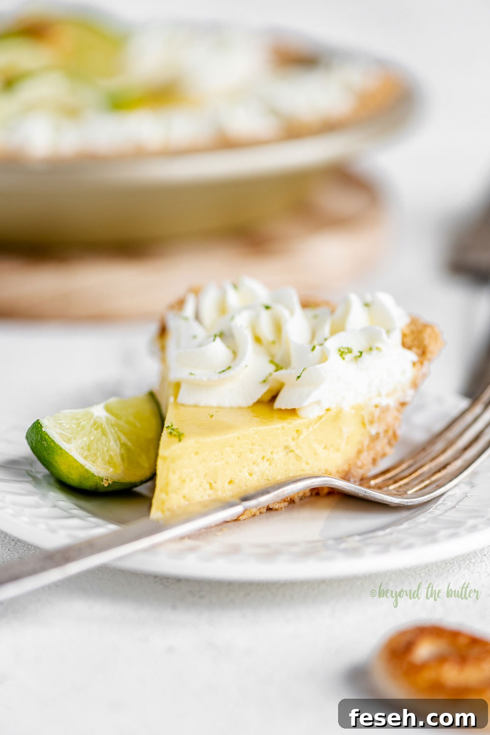 Easy Key Lime Pie decorated with homemade whipped cream, puff pastry twists, and sliced limes | Image and Copyright Policy: © Beyond the Butter, LLC