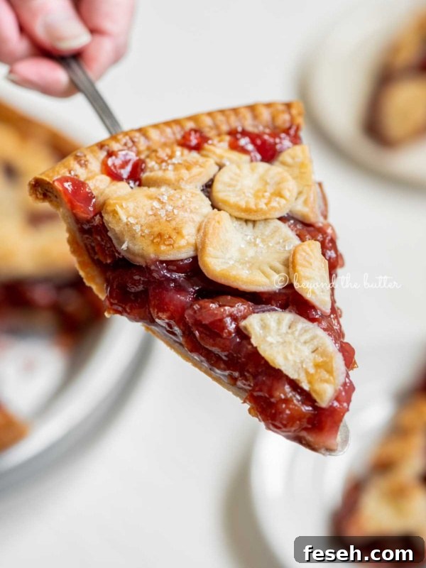 Hand holding a slice of homemade cherry pie with slices in the background.