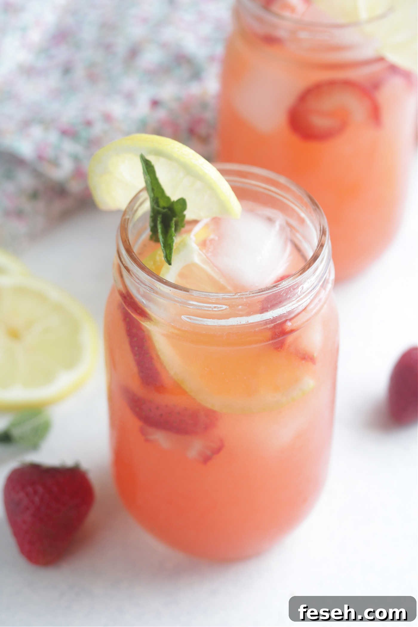 Angled shot of strawberry lemonade spritzers with sliced lemons and mint leaves in a jar glass