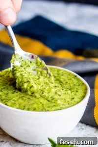Silver spoon dipping into white bowl of chimichurri sauce.