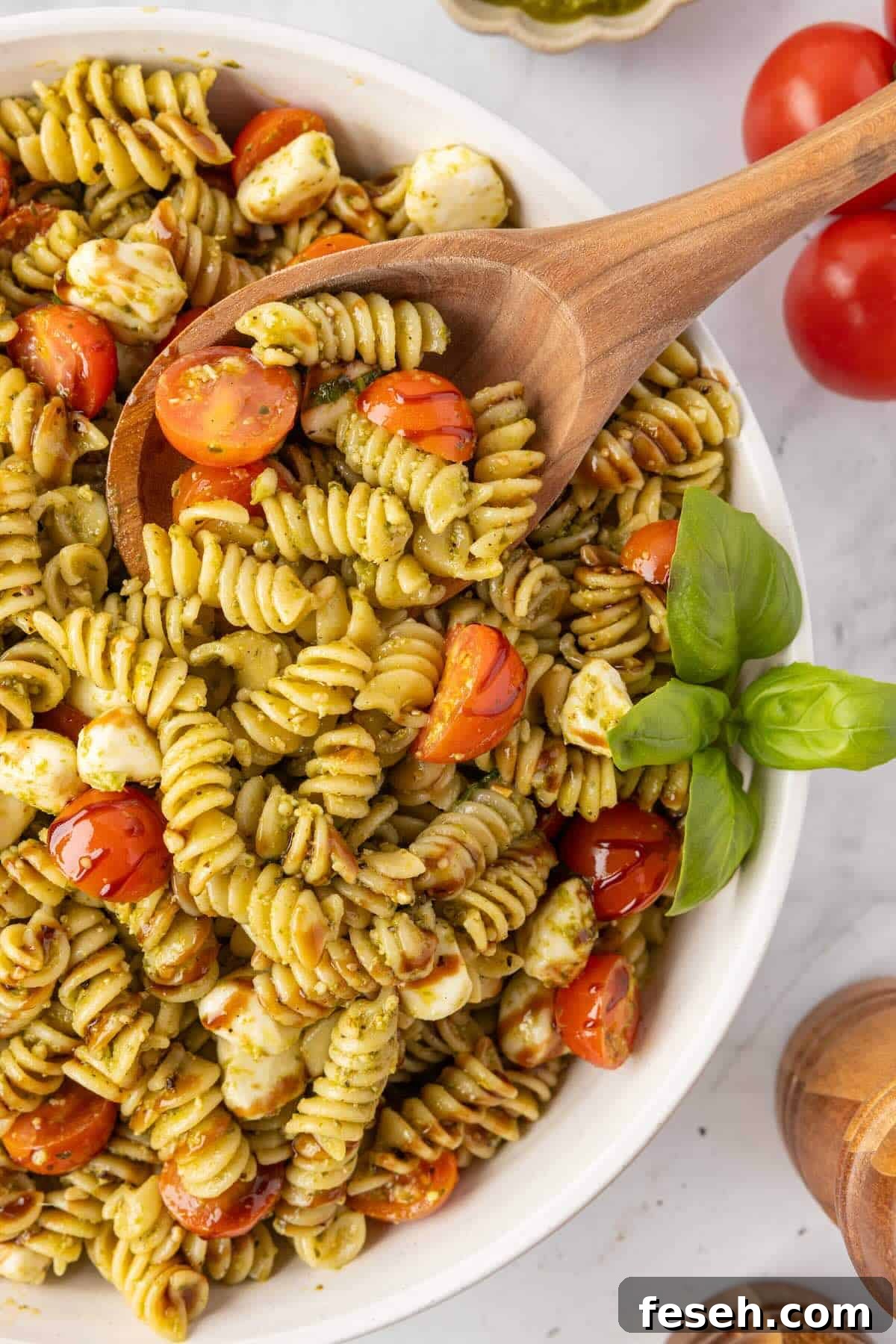 Caprese pasta salad made with rotini, cherry tomatoes, mozzarella pearls, fresh basil, and a drizzle of balsamic glaze in a white bowl.