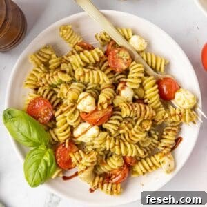A serving of Caprese pasta salad on a white plate with a fork and fresh basil garnish.