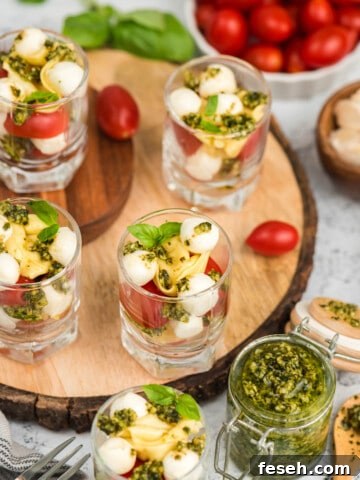 Tortellini Caprese salad cups on a wooden slab surrounded by fresh pesto.