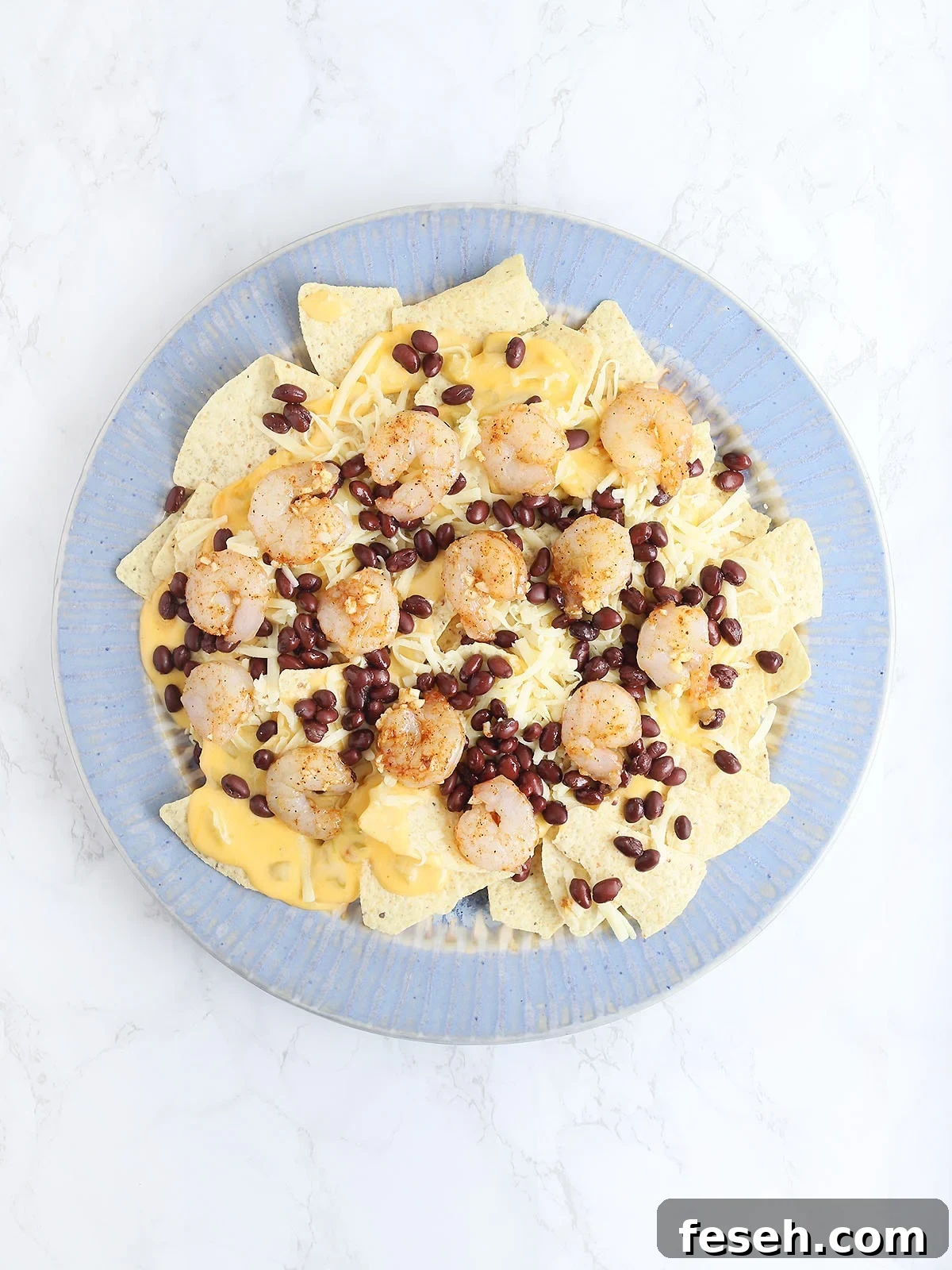 blue platter topped with tortilla chips, chili cheese sauce, Monterrey Jack cheese, black beans and uncooked shrimp