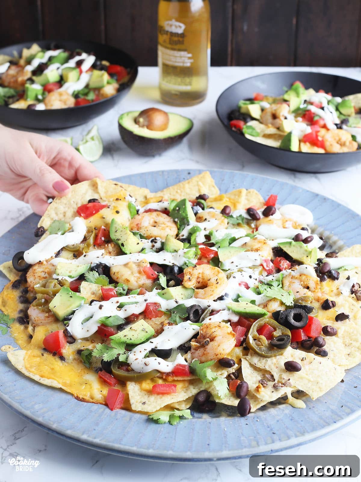 hand reaching for a chip from a large blue platter of shrimp nachos