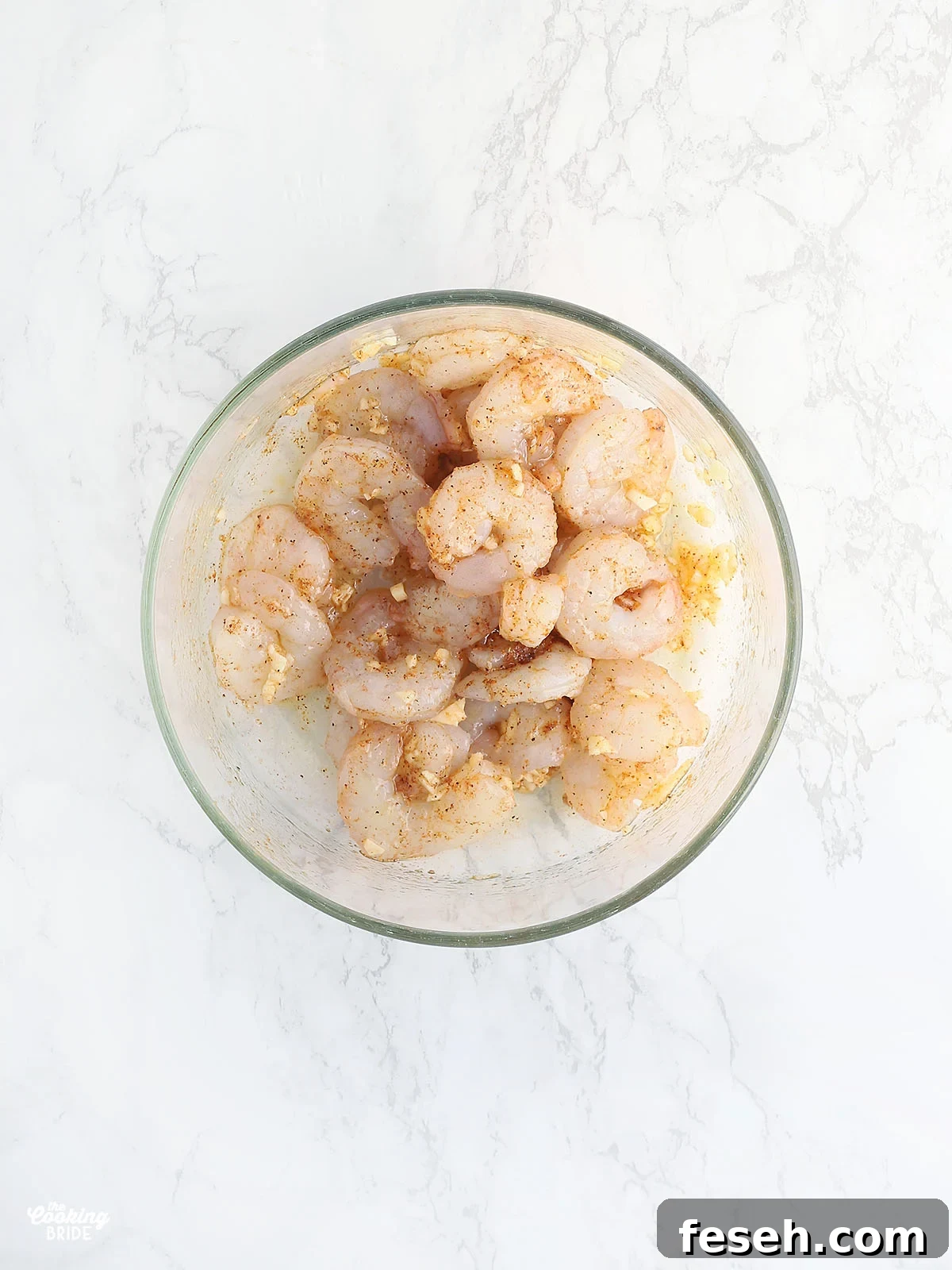 shrimp seasoned with olive oil, minced garlic and Cajun seasoning in a glass bowl