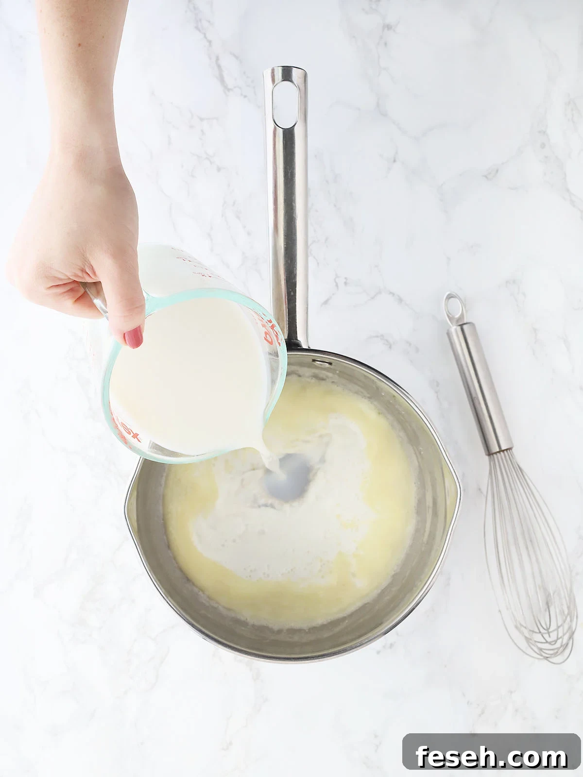 hand pouring milk into a saucepan with melted butter and flour