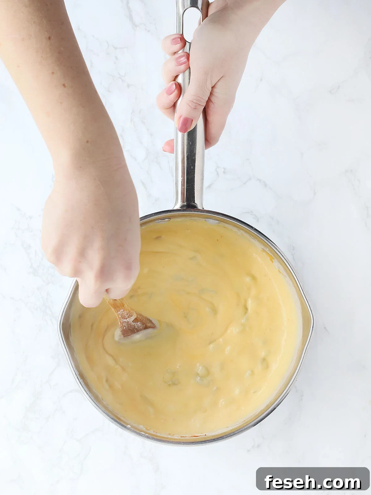 hands stirring a pan of chili cheese sauce
