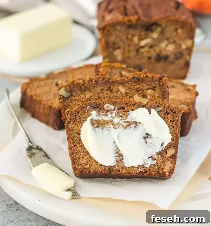 slice of paleo pumpkin bread spread with butter and more bread slices behind it