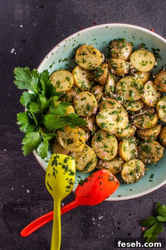 chimichurri potato salad in a bowl with two serving spoons and parsley garnish