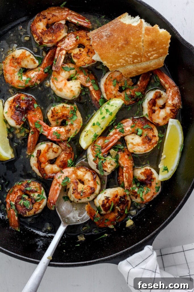 A cast iron skillet with seared shrimp, herbs, lemon wedges and crusty bread.