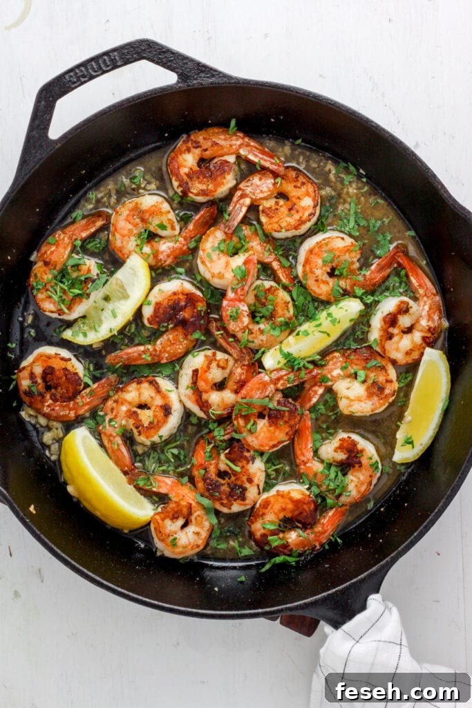 Skillet with seared shrimp, white wine sauce, herbs and lemon wedges.