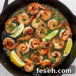 Skillet with seared shrimp, herbs, wine sauce and lemon wedges.
