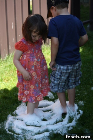 toddler and preschooler standing in soapy water on grass