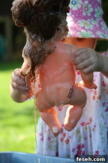 toddler holding doll over basin of water