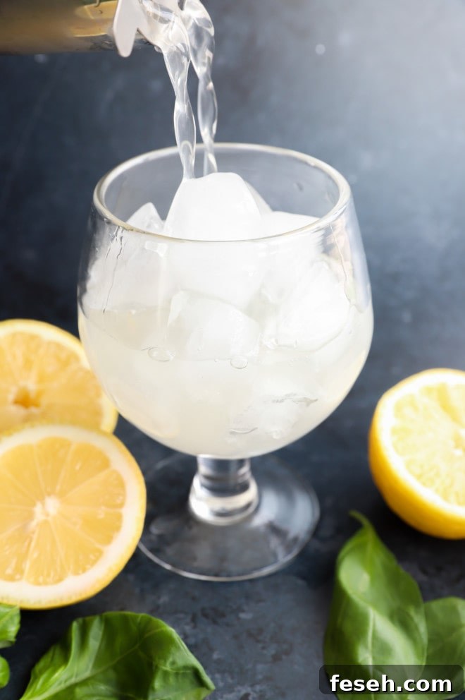 Pouring into glass lemon drink with fresh herbs