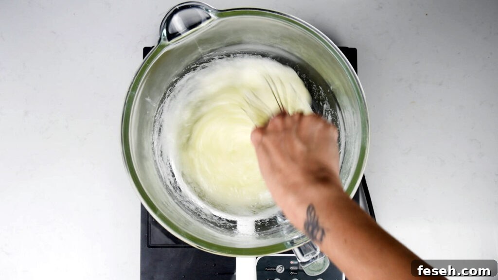 A person whisking a white mixture for meringue in a glass bowl.
