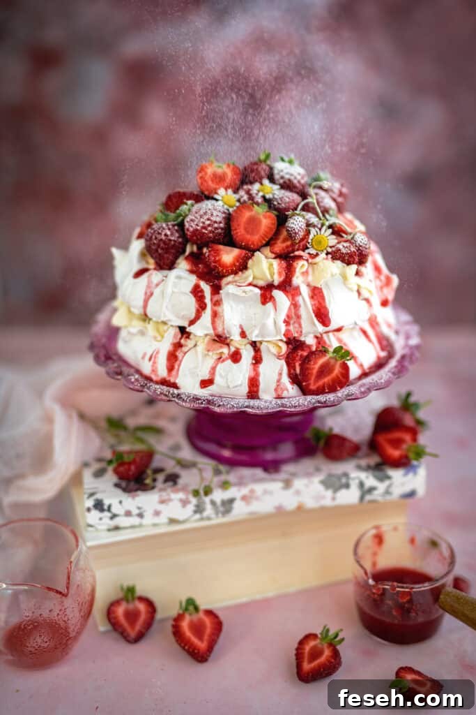 A two-layer meringue cake topped with whipped cream, fresh strawberries, and a drizzle of red sauce, displayed on a pink cake stand.