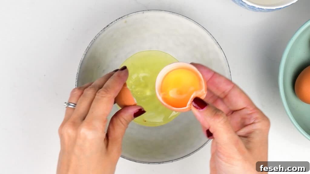 Hands cracking a brown egg over a white bowl, showing yolk and white.