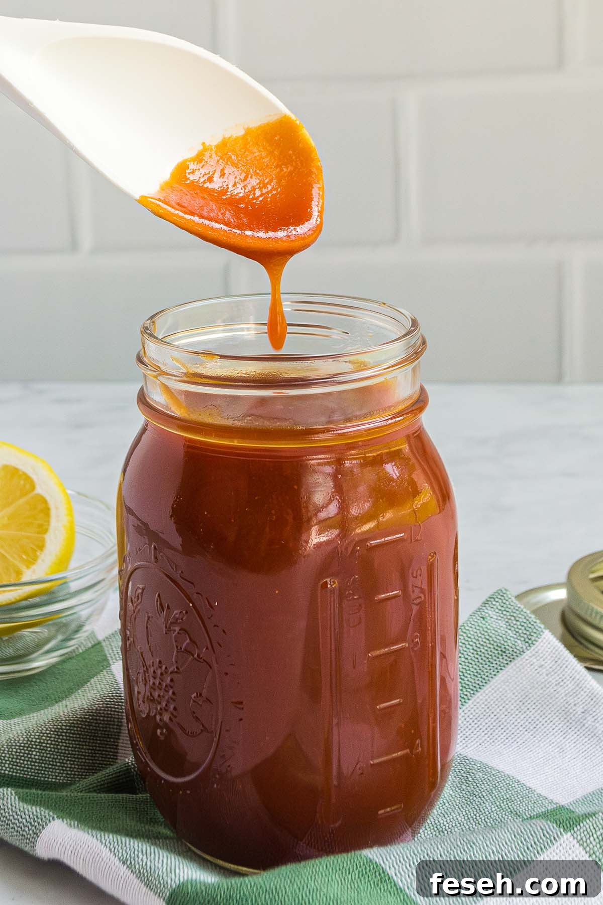 A jar with a spoon dripping homemade bbq sauce.