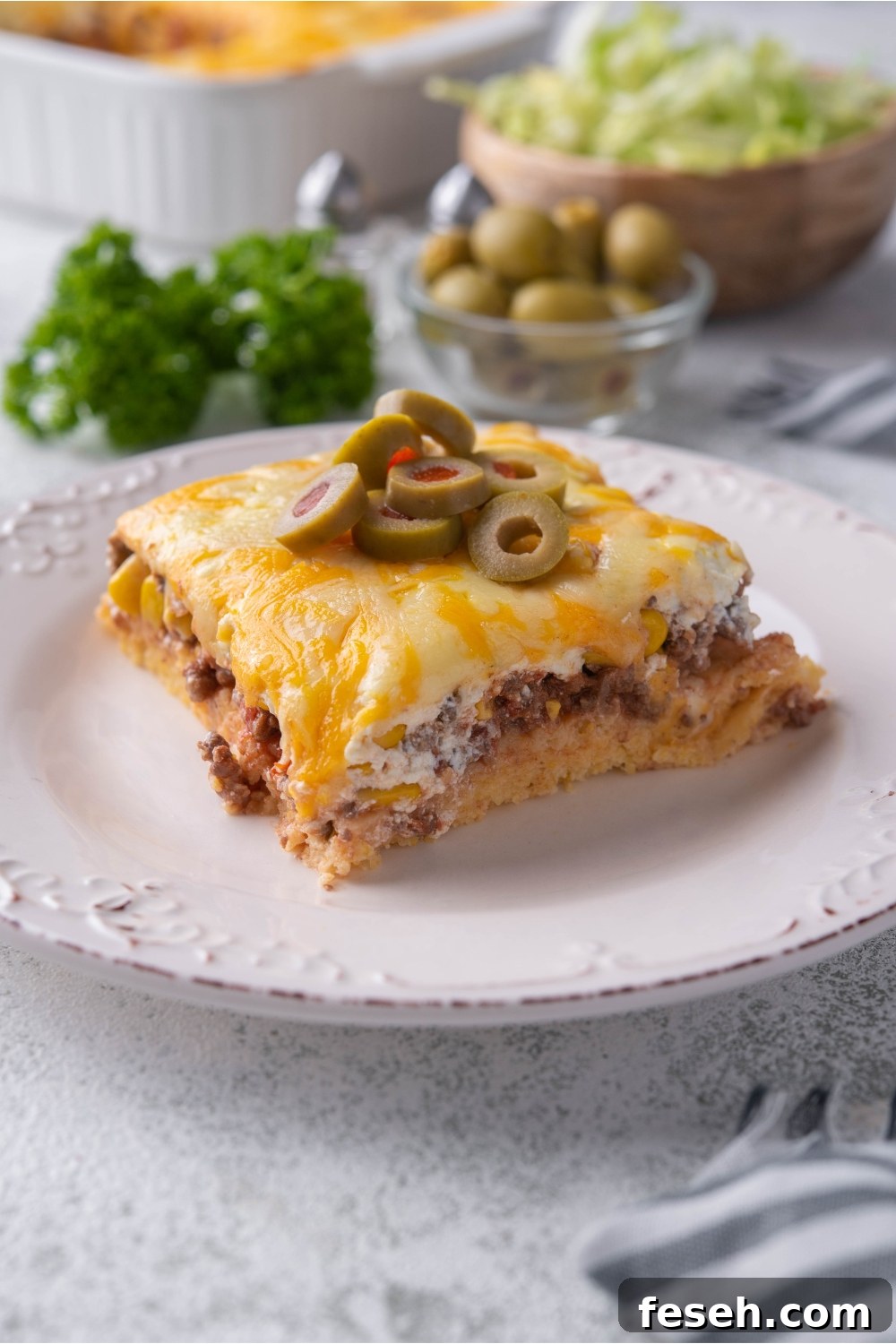 A serving of cornbread taco casserole on a white plate with sliced green olives garnish