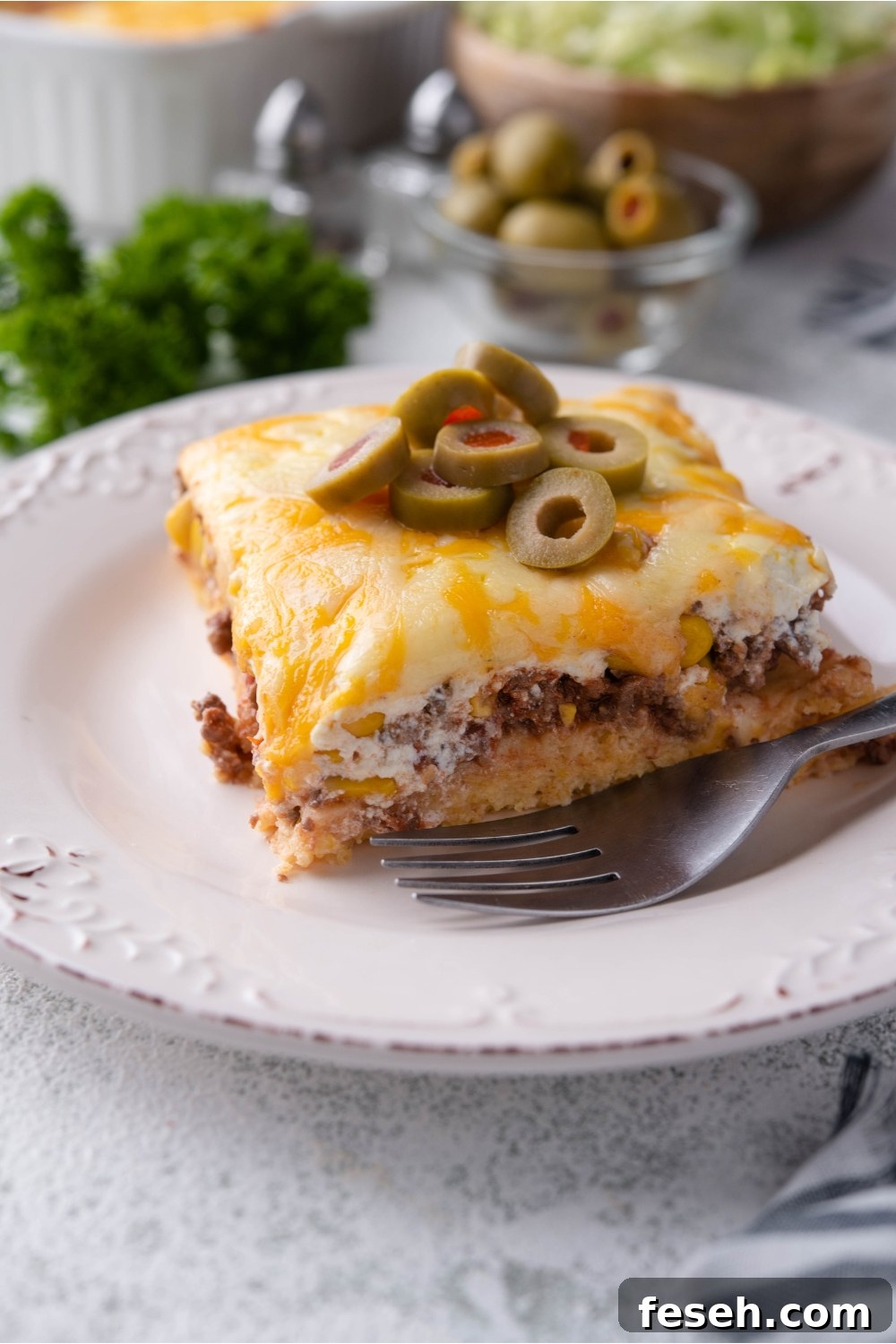 A serving of cornbread taco casserole on a white plate with sliced green olives and a fork