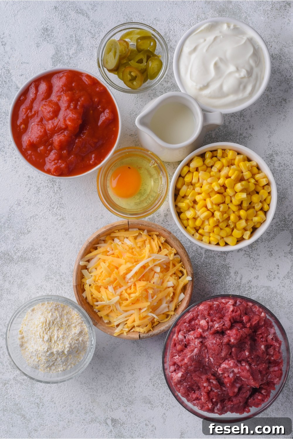 Overhead view of ingredients including sour cream, egg, cornbread mix, tomatoes, corn, ground beef, and shredded cheese