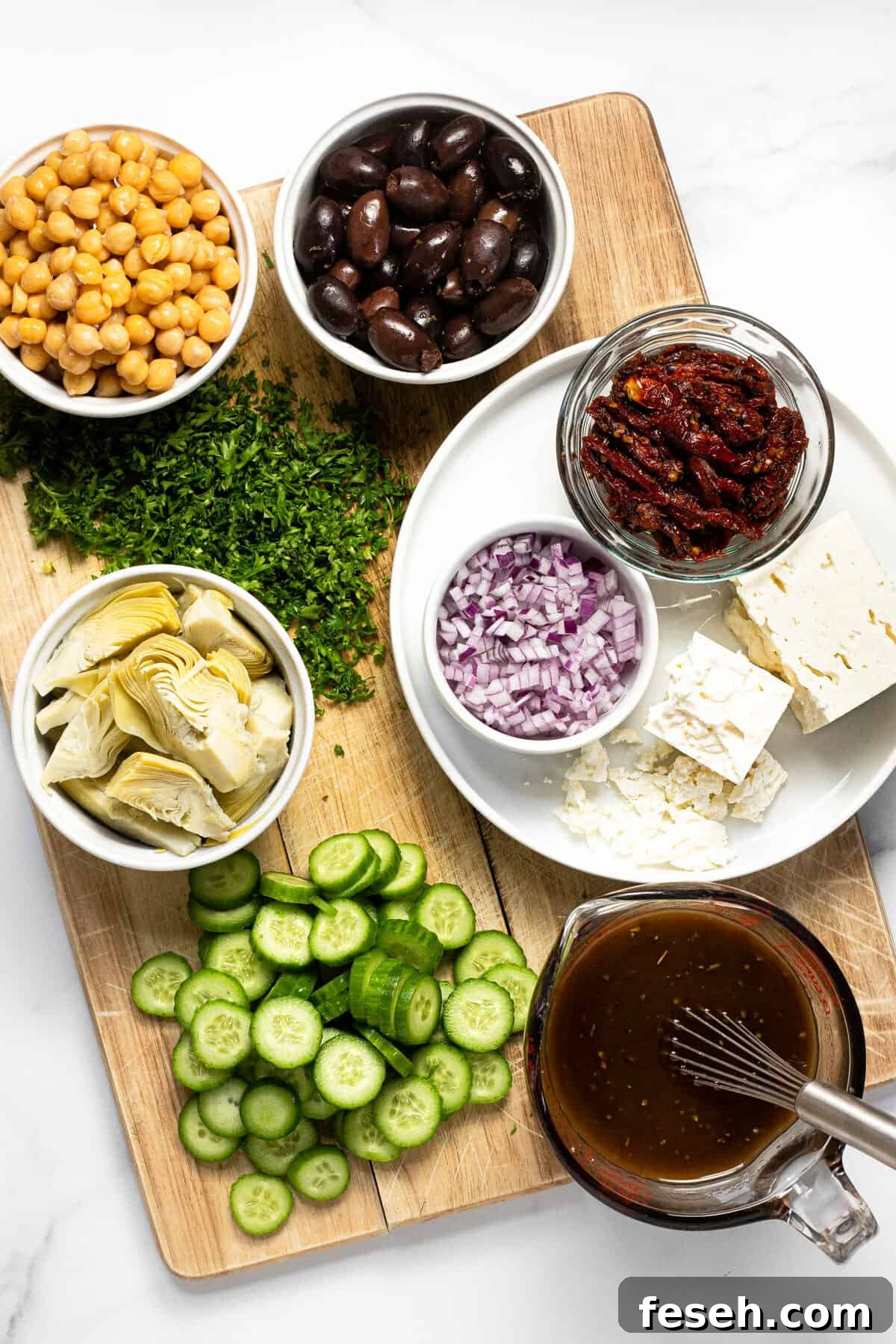 Wooden cutting board with ingredients to make Greek orzo salad on it