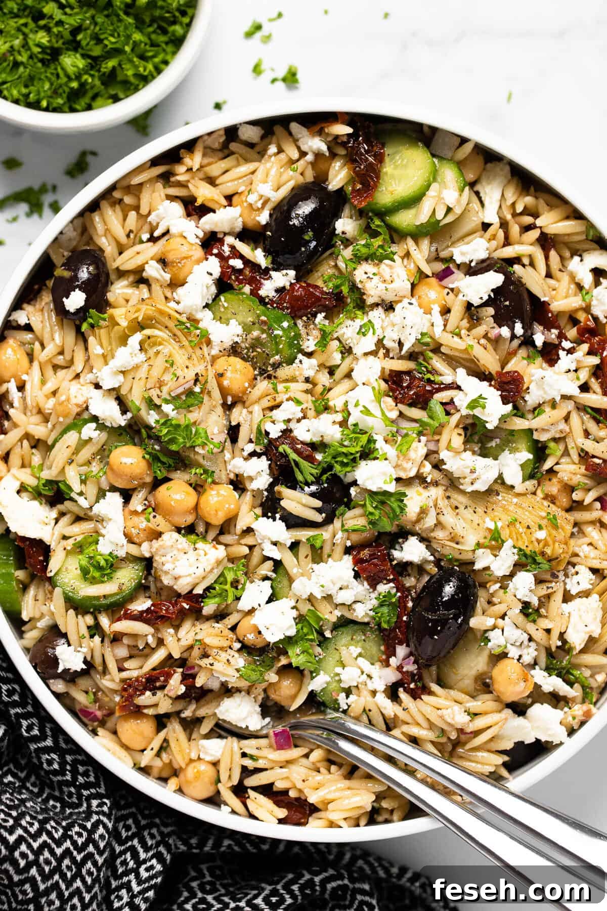 Large white bowl filled with Greek pasta salad garnished with parsley 